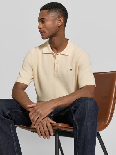 Męski model nosi Regular Fit Poloshirt mit Label-Stitching od Gant z bawełny, kołnierzyk polo, jasny kolor, widoczna tekstura, ujęcie z boku, długość tyłu w rozmiarze M: 68 cm, krój regular fit.