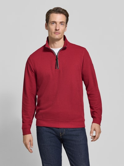 Männermodel trägt Relaxed Fit Sweatshirt aus Baumwoll-Mix Modell 'SELANIK' von LERROS in Rot, dezente Struktur, Ganzkörperansicht von vorne. Rückenlänge 68 cm, Ärmellänge 65 cm, Troyer-Kragen, elastische Abschlüsse.