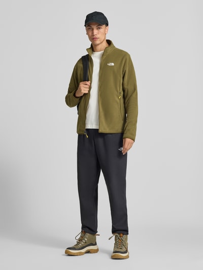 Męski model nosi kurtkę z polaru z zamkiem błyskawicznym Model 'GLACI' od The North Face, krój taliowany, boczne kieszenie zapinane na zamek błyskawiczny, wyhaftowane logo, długość tyłu 66 cm, długość rękawów 68 cm, widok całej sylwetki z przodu.