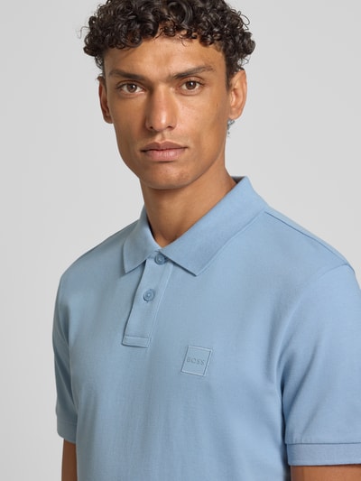 Männermodel trägt Regular Fit Poloshirt aus Baumwoll-Mix Modell 'PASSENGER' von BOSS Orange, Optik: Unifarben, Label-Stitching-Applikation, Polokragen, V-Ausschnitt, kurze Knopfleiste, Kurzarm, Ärmelabschluss: Gerippt, Materialverarbeitung: Piqué, Nahaufnahme Oberkörper.