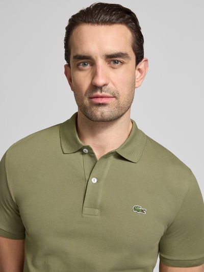 Männermodel trägt Slim Fit Poloshirt aus reiner Baumwolle von Lacoste, jednolity kolor, krój slim fit, wyhaftowane logo, kołnierzyk polo, krótki rękaw, prążkowane zakończenie rękawów, wykończenie z bocznymi rozcięciami, pika, bawełna, Nahaufnahme Oberkörper.