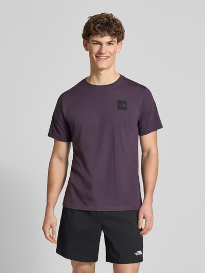 Männermodel trägt T-Shirt aus Baumwoll-Mix Modell 'EVOLUTION' von The North Face in Dunkellila mit Label-Print, Ganzkörperansicht von vorne.