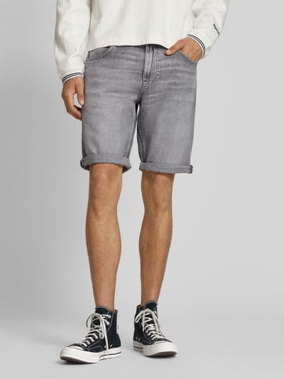 Męski model nosi Regular Fit Jeansshorts aus Baumwoll-Mix od Tommy Jeans, stylizowana na denim, mieszanka bawełny, 5 kieszeni, naszywka z logo i wyhaftowane logo, szlufki na pasek, zapięcie na guzik i ukryty zamek błyskawiczny, widok z przodu na całe ciało.