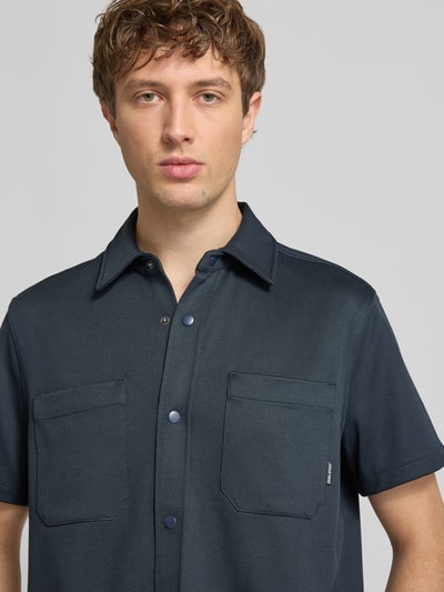 Männermodel trägt Regular Fit vrijetijdsoverhemd met borstzak model 'ADRIAN' van Blend in donkerblauw, elastische materiaalmix met viscose, kentkraag, knoopsluiting, borstzakken, maat M: ruglengte 71 cm, schouderbreedte 47 cm, mouwlengte 23 cm, textuur glad, kleur effen, nahaufnahme bovenlichaam.