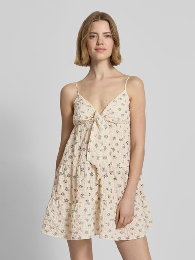 Frauenmodel trägt Minikleid mit Volantsaum und Spaghettiträgern von REVIEW mit floraler Allover-Print, Seersucker, A-Linie, V-Ausschnitt, Knotendetail; cremefarben, leichte Textur, Ganzkörperansicht von vorne.