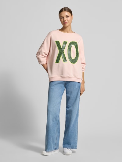 Frauenmodel trägt Oversized Sweatshirt mit Pailettenbesatz Modell 'XO' von miss goodlife in Rosa, reine Baumwolle, Ganzkörperansicht von vorne.