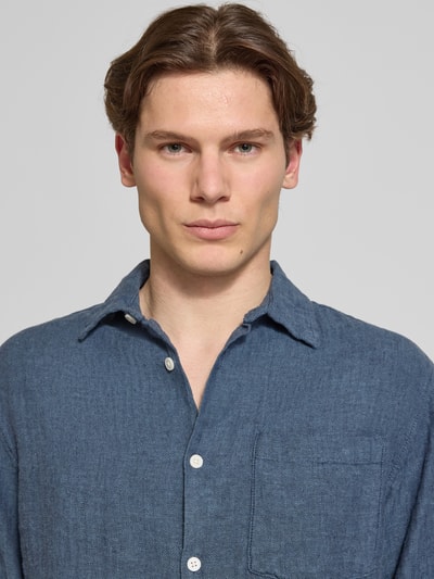 Männermodel trägt blaues Slim-Fit Freizeithemd aus Leinen-Baumwoll-Mix Modell 'NELSON' von Redefined Rebel mit Brusttasche, Nahaufnahme Oberkörper. Rückenlänge 50 cm, Schulterbreite 49 cm, Ärmellänge 72 cm. Label-Detail sichtbar.