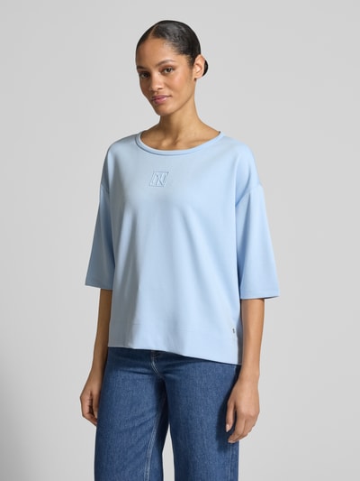 Frauenmodel trägt Damen T-Shirt mit Rundhalsausschnitt und Logo von monari in Hellblau, Relaxed-Fit, Material-Mix mit Viskose-Anteil, Ganzkörperansicht von vorne.