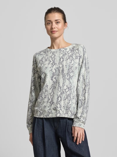 Frauenmodel trägt Comfort Fit Sweatshirt aus Baumwoll-Mix von Tom Tailor Denim mit abstraktem Allover-Muster, Rundhals, Raglanärmel, Logo-Applikation, helle Grau- und Blautöne, weiche Struktur, Ganzkörperansicht von vorne.