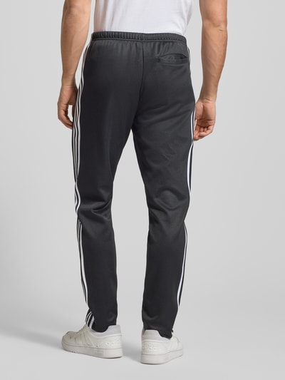 Männermodel trägt Sweatpants mit elastischem Bund von adidas Originals in Schwarz mit weißen Streifen, lockerem Schnitt und Gesäßtasche, Baumwoll-Mix. Ganzkörperansicht Rückansicht.