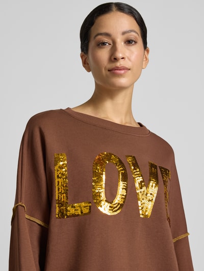 Frauenmodel trägt Oversized Sweatshirt aus reiner Baumwolle Modell 'LOVE' von miss goodlife in Braun mit goldfarbenem Pailletten-Print, Nahaufnahme Oberkörper.