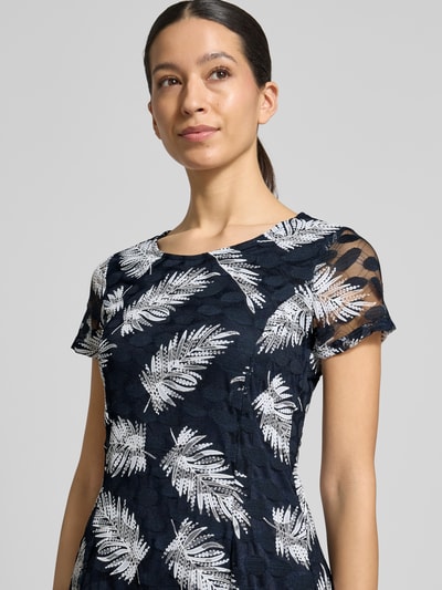 Vrouwenmodel draagt knielanges Kleid mit Rundhalsausschnitt van Apricot in donkerblauw met witte bladprint, getailleerde fit, stretch-materiaal, korte mouwen, detailopname bovenlichaam.