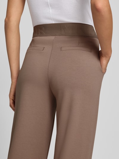 Vrouwenmodel draagt Straight Fit broek van viscosemix met logodetail van monari in taupe, elastische band, siernaden, detailopname rug. Context: dames broek van monari, elastische materiaalmix met viscose, straight fit, logodetail, elastische band, siernaden, bandwijdte maat 36: 38 cm, binnenbeenlengte maat 36: 79 cm.
