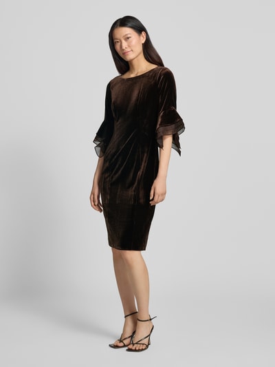 Frauenmodel trägt Abendkleid aus Samt mit Rundhalsausschnitt von Adrianna Papell, dunkelbraun, tailliert, mittellang, Ganzkörperansicht von vorne. Material-Mix mit Stretch-Anteil, rückseitiger Reißverschluss, Rücklänge 100 cm, Brustweite 41 cm, Ärmellänge 45 cm.
