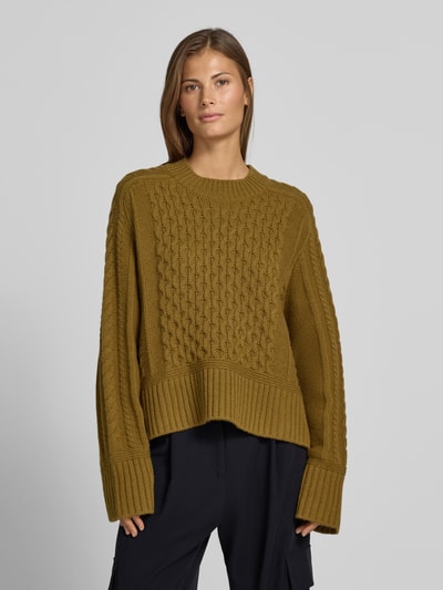 Frauenmodel trägt Strickpullover mit Zopfmuster von Style Icon Collection in Olivgrün, lockere Passform, Rundhalsausschnitt, reine Baumwolle, gerippte Abschlüsse, Ganzkörperansicht von vorne.