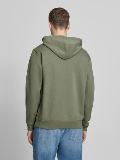 Männermodel trägt Hoodie mit Kängurutasche von GAP in Olivgrün, Baumwoll-Mix, lockere Passform, Ganzkörperansicht Rückansicht.