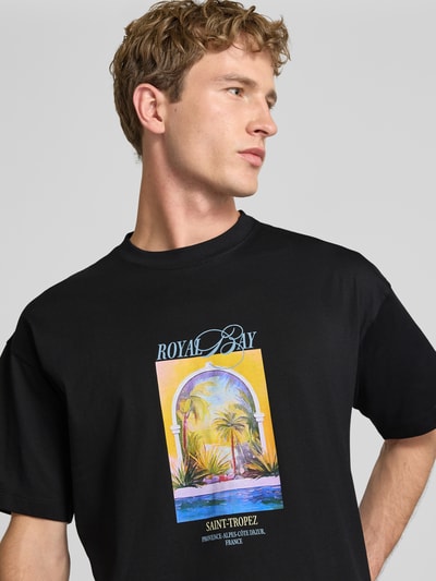 Männermodel trägt T-Shirt mit Motiv-Print Modell 'SANREMO' von JACK & JONES, schwarz, bunter Print, reine Baumwolle, Regular Fit, Nahaufnahme Oberkörper.