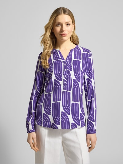 Frauenmodel trägt Wellen-Print Schlupfbluse aus Viskose von Christian Berg Woman, Regular-Fit, V-Ausschnitt, weiß-lila Muster, Ganzkörperansicht von vorne.