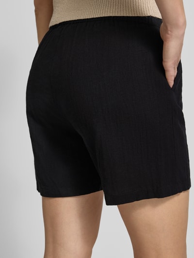 Frauenmodel trägt Regular Fit Bermudas aus reiner Baumwolle Modell 'TIZANA' von Only, schwarze Flammgarn-Optik, Ganzkörperansicht Rückansicht.