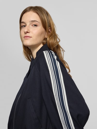 Frauenmodel trägt Regular Fit Sweatjacke mit Viskose-Anteil von Marc O'Polo Denim in Dunkelblau mit weißen Kontraststreifen, Nahaufnahme Oberkörper. Unifarbene Optik, Reißverschluss, seitliche Eingrifftaschen, gerippte Abschlüsse, Umlegekragen, Label Stitching.