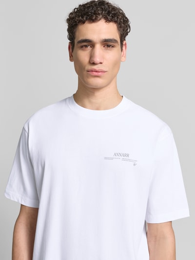 Männermodel trägt Relaxed Fit T-Shirt aus reiner Baumwolle von ANNARR in Weiß mit Label-Print, Kurzärmelig, Rundhalsausschnitt, Nahaufnahme Oberkörper. Herren T-Shirt, Rückenlänge bei Größe M 67 cm.