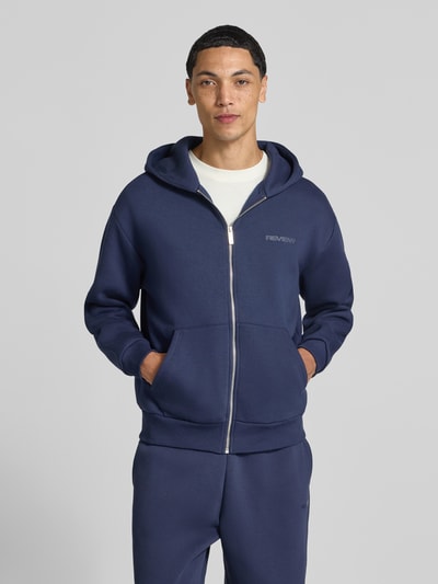Männermodel trägt Sweatjacke aus Baumwoll-Mix von REVIEW in Dunkelblau, lockere Passform, Kängurutasche, Ganzkörperansicht von vorne.