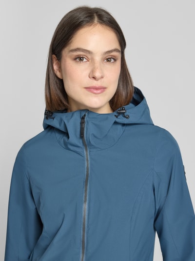 Frauenmodel trägt Regular Fit Regenmantel mit Logo-Detail von G.I.G.A. DX in Blau mit Kapuze und Zweiwege-Reißverschluss, Nahaufnahme Oberkörper