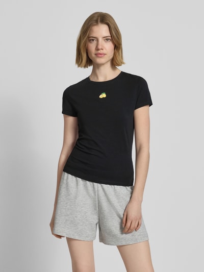 Frauenmodel trägt Slim Fit T-Shirt mit Motiv-Stitching von REVIEW aus elastischem Baumwoll-Mix in Schwarz mit Rundhalsausschnitt, Rückenlänge 55 cm, Ganzkörperansicht von vorne.