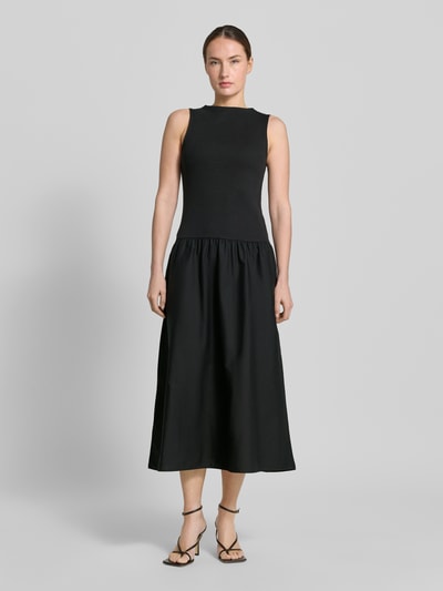 Frauenmodel trägt Damen Midikleid mit U-Boot-Ausschnitt Modell 'VALVIN' von Mango, schwarzer Baumwoll-Mix mit Stretch-Anteil, Taillierter Schnitt, Ganzkörperansicht von vorne.