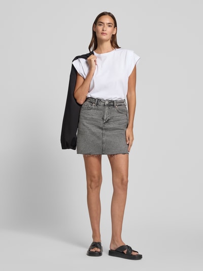 Vrouwenmodel draagt Regular Fit jeansrok uit katoenmix model 'TESSA' van Vero Moda in grijze denimlook met labelpatch, minilengte, 5-pocketmodel, riemlussen, knoop- en ritssluiting, twillmateriaal, vooraanzicht volledige lichaamsweergave.