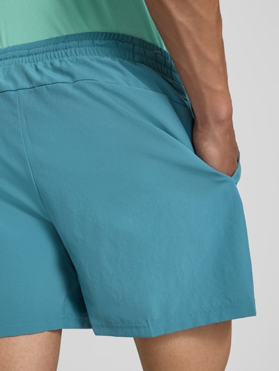 Männermodel trägt Shorts mit elastischem Bund und Logo von New Balance in Blau, Regular-Fit, Detailaufnahme Rückansicht. Bundweite 39 cm, Innenbeinlänge 12 cm, Tunnelzug, Logo.