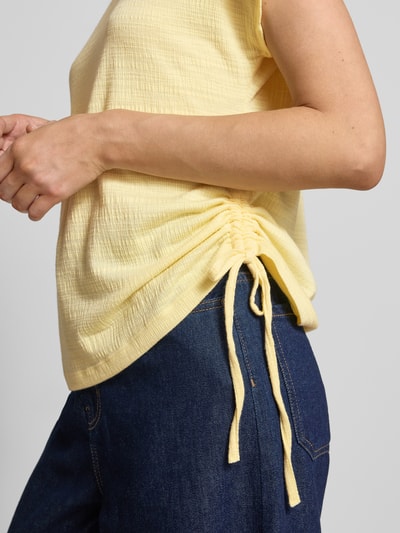Frauenmodel trägt Regular Fit T-Shirt mit Viskose-Anteil von Apricot, gelb, Strukturmuster, Zierschleifen, Nahaufnahme Oberkörper.
