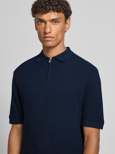 Mężczyzna nosi Regular Fit Poloshirt aus reiner Bio-Baumwolle Modell 'CRAN' von SELECTED HOMME w granatowym kolorze, strukturalna dzianina, krótki rękaw, kołnierzyk polo, z krótkim zamkiem, widok na górną część ciała z przodu.