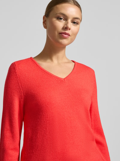 Frauenmodel trägt Regular Fit Longsleeve aus Viskose in Strick-Optik Modell 'Viril' von Vila in leuchtendem Korallrot, V-Ausschnitt, Nahaufnahme Oberkörper.