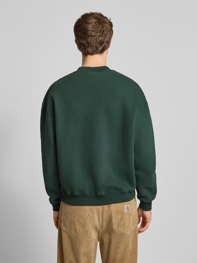Männermodel trägt Sweatshirt mit Logo und Rundhalsausschnitt von BLKVIS in Dunkelgrün aus reiner Baumwolle im Relaxed-Fit, Ganzkörperansicht Rückansicht. Rückenlänge bei Größe M 66 cm, Ärmellänge 61 cm.
