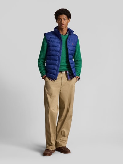 Männermodel trägt Regular Fit Weste mit Logo-Stitching von Polo Ralph Lauren in Blau, kombiniert mit grüner Kleidung, Ganzkörperansicht von vorne.