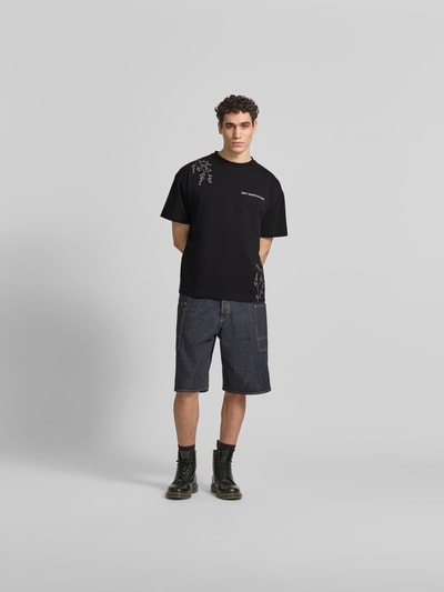 Männermodel trägt Relaxed Fit T-Shirt aus Baumwoll-Mix von Don’t Waste Culture, Schwarz, Rundhalsausschnitt, Motiv-Print, Label-Print, Rückenlänge 70 cm bei Größe M, Ganzkörperansicht von vorne.