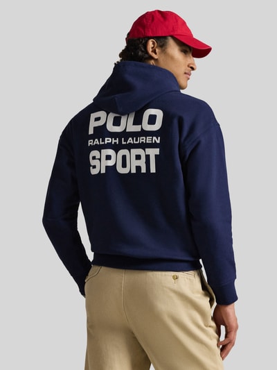 Männermodel trägt Relaxed Fit Hoodie aus katoenmix van Polo Ralph Lauren in effen donkerblauw met labelprint, kangoeroezak, capuchon met tunnelkoord, lange mouwen, geribde rompzoom en mouwboorden, sweatmateriaal. Ganzkörperansicht Rückansicht.