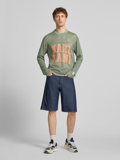 Männermodel trägt Longsleeve mit Label-Patch und Rundhalsausschnitt von KARL KANI, Boxy-Fit, Logo-Print, Rückenlänge 63 cm, Ganzkörperansicht von vorne.