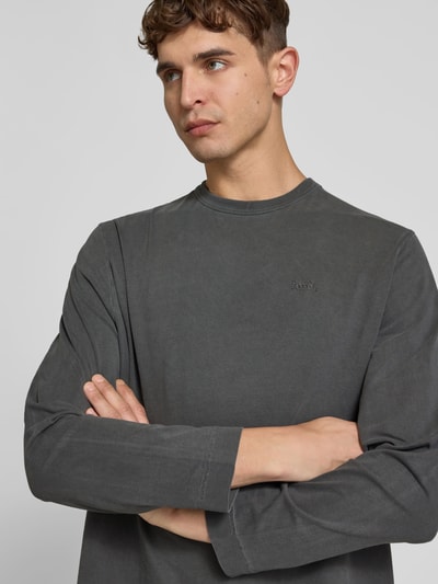 Männermodel trägt Relaxed Fit Longsleeve aus Baumwolle von Forét in Grau mit Rundhalsausschnitt, Used-Look, Label-Stitching, Nahaufnahme Oberkörper.