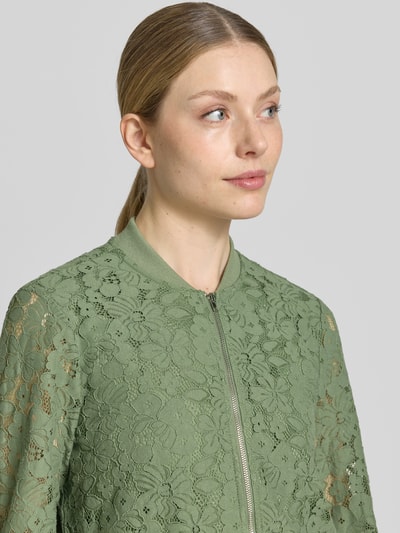 Frauenmodel trägt Regular Fit Blouson aus Baumwoll-Mix Modell 'HONEY' von Vero Moda mit Florales-Allover-Muster, Reißverschluss, Optik: Allover-Muster, in grün mit gehäkelter Textur, Nahaufnahme Oberkörper.