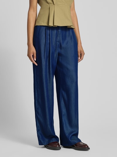 Kobieta nosi Wide Leg Jeans aus Lyocell od s.Oliver BLACK LABEL, tkanina stylizowana na denim, krój wide fit, zakładki w pasie, elastyczny ściągacz, wpuszczane kieszenie, imitacja kieszeni z tyłu, materiał: lyocell, widok całej sylwetki z przodu.