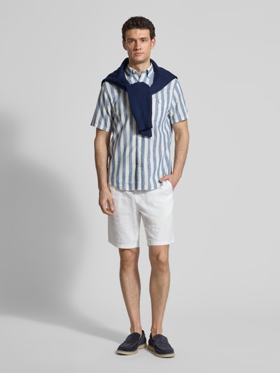Męski model nosi Regular Fit Freizeithemd aus Leinen-Baumwoll-Mix von Gant, niebieskie i białe paski, kołnierz button-down, kieszeń na piersi, szwy z logo, krój regular fit, widok całej sylwetki z przodu.