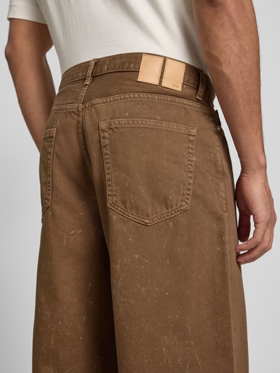 Mężczyzna ma na sobie jeansy z kieszeniami wpuszczanymi Jeans mit Eingrifftaschen Modell 'Type 3' od Wood Wood, bawełna, krój relaxed fit, kolor brązowy, Szerokość w rozmiarze 32/32: 44 cm, długość wewnętrzna nogawki: 75 cm, zbliżenie na tylne kieszenie, ujęcie z tyłu.