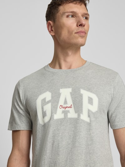 Männermodel trägt T-Shirt mit Logo und Rundhalsausschnitt von GAP in Grau, Reine Baumwolle, Regular-Fit, Rückenlänge 69 cm, Nahaufnahme Oberkörper.