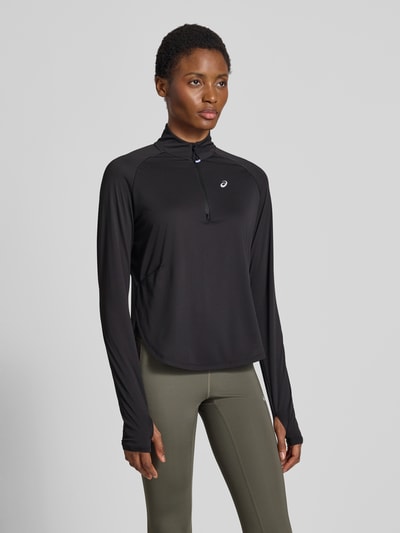 Frauenmodel trägt Longsleeve mit Troyer-Kragen Modell 'NAGINO' von ASICS TIGER in Schwarz, reflektierendes Logo, Raglanärmel, Ganzkörperansicht von vorne.
