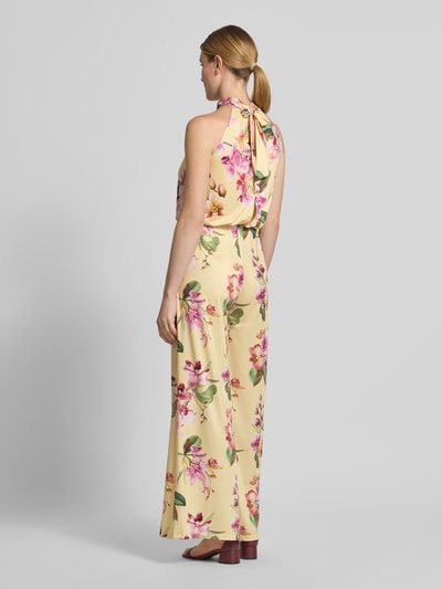 Modelka nosi Regular Fit Jumpsuit mit floralem Allover-Print von V by Vera Mont, żółty z różowymi i zielonymi kwiatami, krój regular fit, detal cut-out na plecach, zamek na szwie, bez rękawów, długość tyłu w rozmiarze 36: 147 cm, szerokość w rozmiarze 36: 36 cm, całkowita długość w rozmiarze 36: 132 cm, długość wewnętrzna nogawki w rozmiarze 36: 81 cm, widok całej sylwetki z tyłu