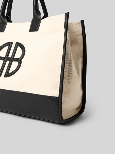Produktfoto, Tote Bag mit Logo-Detail von Anine Bing aus cremefarbenem Material mit schwarzem Strukturmuster, Magnetverschluss, abgerundete Tragehenkel, Reißverschlussfach innen, Hauptfach, Maße: 49 cm Breite, 29 cm Länge, 13 cm Tiefe.