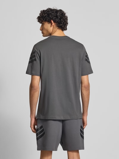 Männermodel trägt Relaxed Fit T-Shirt aus reiner Baumwolle von adidas Sportswear in Optik: Unifarben mit Logo-Print, Ganzkörperansicht Rückansicht.