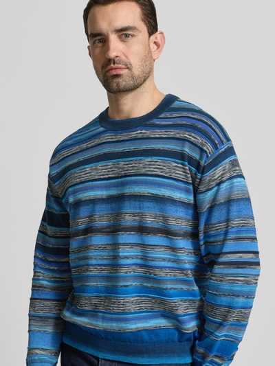 Männermodel trägt Strickpullover im Allover-Look mit Rundhalsausschnitt von PAUL SMITH, Blau- und Grautöne, reine Baumwolle, Nahaufnahme Oberkörper.